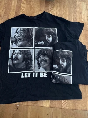 Svart Let It Be t-shirt med tryck - Två svarta t-shirtsr med grafiskt tryck på framsidan som visar  porträtt och texten 'LET IT BE'  Perfekt för dig som gillar musik och vill sticka ut med en ikonisk design. Tröjorna är använda endast en gång och är i extremt bra skick. Tröjorna säljs tillsammans.