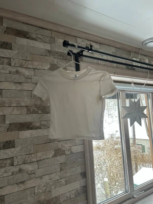 Vit croppad t-shirt från H&M Divided - En enkel och stilren vit croppad t-shirt från H&M Divided. T-shirten har rund halsringning och korta ärmar. Tillverkad i mjuk bomull som känns skön mot huden. Perfekt till jeans eller kjol för en clean look.