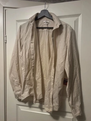 Beige skjorta från Jack & Jones - Säljer en stilren beige skjorta från Jack & Jones Premium i slim fit. Skjortan har klassisk krage, långa ärmar och knappar framtill. Perfekt att bära öppen över t-shirt eller stängd för en clean look.