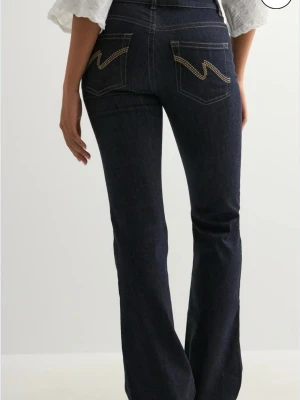 Mörkblå mid waist bootcut jeans med kontrastsömmar - Säljer ett par mörkblå jeans från Nelly med bootcut passform och snygga kontrastsömmar. Bakfickorna har ett coolt broderat zigzag-mönster i beige. Jag beställde fel storlek då den kommer inte till användning. Har använt den några gånger bara o köpte den för 700, skriv för egna bilder 💗💗💗