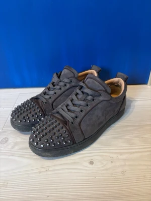 Mörkgrå mocka sneakers med nitar - Tjena säljer dessa asfeta skor från louboutin. Skorna har nitar där fram och är i grå färg. Pris kan diskuteras. Skriv vid minsta frågor eller prisförslag❤️Skorna är i storlek 42 men passar mig som har storlek 43.  (Obs en nit är av)