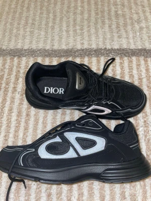 Svarta Dior B30 sneakers utan box - Säljer ett par svarta Dior B30 sneakers med reflekterande detaljer och tydlig CD-logga på sidan. Skorna har snörning, mesh och syntetmaterial samt en chunky sula. Tillverkade i Italien och riktigt snygga till streetwear eller casual outfits.