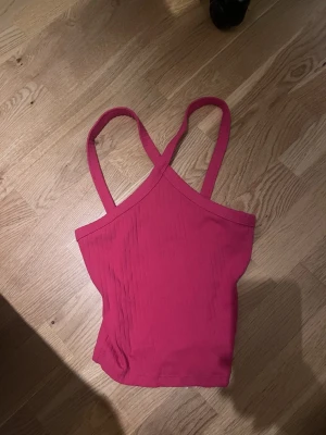 Rosa ribbad linnetopp - Säljer en snygg rosa linnetopp med ribbad struktur och smala axelband som korsas i ryggen. Toppen är croppad och har en enkel, stilren design som passar perfekt till sommaren. Materialet känns mjukt och stretchigt, troligen bomull eller polyester.