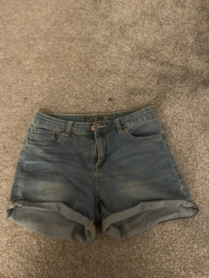 Blå jeansshorts från Amisu - Säljer ett par klassiska blå jeansshorts från Amisu i storlek 36. De har upprullade benslut, fem fickor och stängs med knapp och dragkedja. Perfekta för varma dagar och har en tidlös look som passar till det mesta.