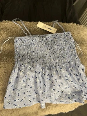 Blommig ljusblå linnetopp Gina Tricot - Supersöt ljusblå linnetopp från Gina Tricot med smala axelband och blommigt mönster i vitt och blått. Toppen har smockad överdel och luftig passform nedtill, perfekt för varma dagar. Tillverkad i mjuk bomull som känns skön mot huden. Prislapp kvar (nypris 229kr)💓
