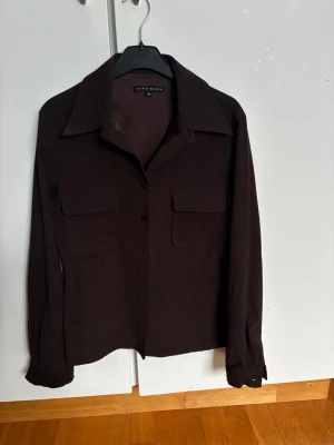 Mocka skjorta från Vero Moda - Säljer en mörkbrun mockaskjorta från Vero Moda i mjukt material. Skjortan har två stora bröstfickor med lock, klassisk krage och knäppning framtill. Mycket fint skick. 