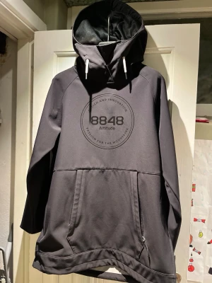 Svart vindjacka, skidjacka, anorak från 8848 Altitude - Säljer en svart vindjacka från 8848 Altitude med stor luva som hjälmen ryms i, stor magficka och dragkedja i sidorna. Jackan har en clean look med logga på bröstet och är fodrad med mjuk fleece på insidan. Perfekt skick, inga tecken på slitage. Kommer från ett djur- och rökfritt hem.