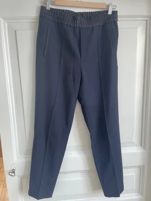 Mörkblå byxor från Filippa K, S - Säljer ett par mörkblå byxor från Filippa K i storlek S. Byxorna har resår i midjan, raka ben och diskreta fickor på sidorna. Materialet känns mjukt och har en dressad look som ändå är chill. Perfekta till sneakers eller boots.