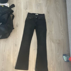 Svarta/gråa bootcut jeans - Snygga svarta/gråa jeans i storlek 34. Modellen har klassisk femficksdesign, medel i midjan och bootcut-ben som ger en schysst siluett. Jeansen är tillverkade i stretchigt denim för skön passform och har svarta sömmar för en clean look.