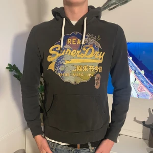Svart Superdry hoodie med tryck - Skön superdry hoodie. Modellen är 187. Mycket bra skick 9/10. Skriv vid funderingar🤗