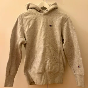 Vintage champion hoodie - Grå hoodie från Champion i storlek Small med klassisk logga på bröstet och ärmen. Tröjan har huva med snörhål, stor magficka och ribbade muddar vid ärmslut och nederkant. 