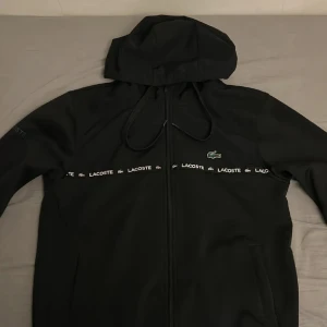 Svart vindjacka från Lacoste med huva - Har använt den ett par gånger. Köpte den för 1600