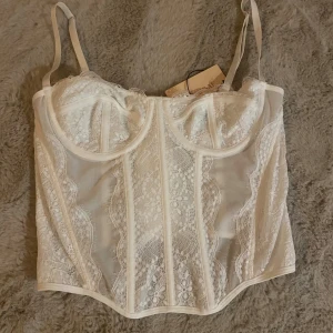 Vit spetskorsett  - Säljer en vit korsett från Shein med vackra spetsdetaljer och transparent mesh. Toppen har reglerbara axelband, formade kupor och hakknäppning i ryggen. Perfekt för dig som vill ha en feminin och trendig look med extra edge.