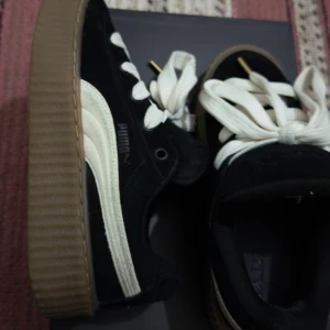 Puma x FENTY Creeper Phatty – Black / Warm White / Gum #4 (Size EU 37) - Selling my authentic Puma x FENTY Creeper Phatty sneakers, designed in collaboration with Rihanna. These stylish shoes feature a black suede upper, warm white Puma stripe, and a gum sole that gives them a bold, iconic look. 	•	Condition: Gently used, excellent condition (see photos) 	•	Size: EU 37 / UK 4 / US 5 / 23 cm 	•	Includes: Original box and extra black laces (unopened) 	•	Retail Price: 1,600 SEK  A perfect blend of street style and comfort – hard to find model!