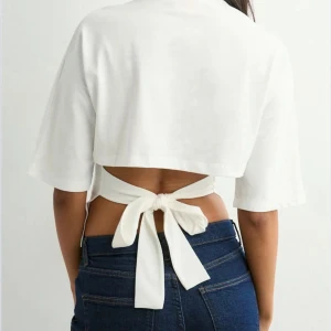 Vit croppad topp med knyt i ryggen - Säljer en vit croppad topp med öppen rygg och breda knytband som knyts i ryggen. Toppen har korta ärmar och är tillverkad i ett mjukt bomullsmaterial. Perfekt för dig som gillar trendiga och avslappnade looks.