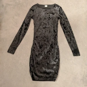 Svart sammetsklänning med lång ärm - Supersnygg svart sammetsklänning med lång ärm och figurnära passform. Klänningen har en kort längd och en mjuk, glansig yta.