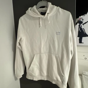 Vit hoodie Around the World Tour hov1    StM  - Säljer en vit hoodie från M1 i storlek M med coolt tryck på ryggen 'Around the World Tour' och en glob i blått och svart. Framtill finns en liten krona broderad på bröstet. Hoodien har snörning, huva och en stor magficka. Perfekt för dig som gillar streetwear.