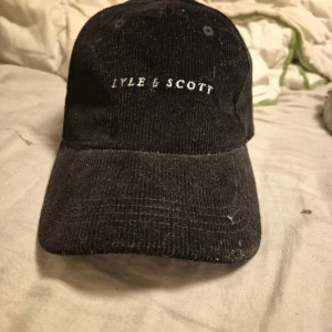 Limited edition Svart manchesterkeps från Lyle & Scott - Snygg svart keps från Lyle & Scott i mjuk manchester med böjd skärm och justerbar rem bak. Klassisk design med broderad logga framtill. Perfekt för dig som vill ha en stilren och cool accessoar till vardagslooken. Limited edition 