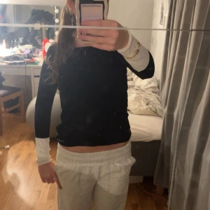 Svart långärmad tröja från Uldahl - Svart långärmad tröja från Uldahl med kontrasterande vita muddar vid ärmsluten. Tröjan har en slim passform och är tillverkad av en mjuk mix av viskos, polyamid, bomull och bambu. Perfekt för dig som gillar stilrena och enkla plagg.