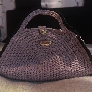 Handgjord rosa stickad handväska - Unik handväska i rosa  med svarta detaljer, stickad i grovt garn. Väskan har en snygg guldig knapp och ett handtag upptill. Perfekt accessoar för dig som vill sticka ut med något personligt och kreativt.