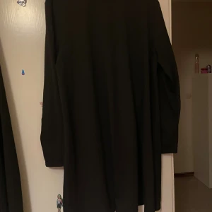 Svart långärmad klänning - En svart långärmad klänning med rund hals och rak passform. Klänningen är enkel och stilren utan mönster eller detaljer, och har en mjuk och följsam känsla i tyget. Perfekt för dig som gillar minimalistisk stil och vill ha något bekvämt och snyggt.