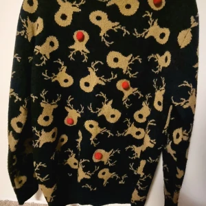 Mörkblå jultröja med renmotiv och röd nosar detaljer - Säljer en mörkblå stickad jultröja med beiga renhuvuden över hela tröjan och röda bollar som markerar renarnas nosar. Perfekt för dig som vill sticka ut på julen! Tröjan har lång ärm och rund hals. Köpt på Next i Storbritannien. 