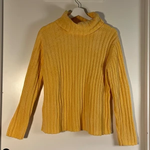 Gul ribbad polotröja Classic Elements - Säljer en gul polotröja från Classic Elements med breda ribbade ränder och mjukt stickat material. Tröjan har lång ärm och hög krage som ger en chill vibe. Perfekt för dig som gillar färg och vill ha något mysigt till hösten.