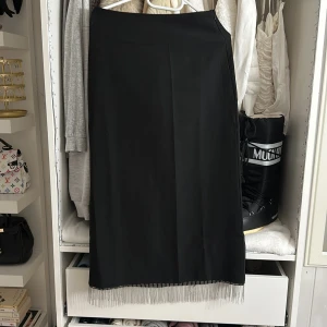 Svart långklänning med silverfransar - Svart långklänning från Vero Moda med stilrena linjer och snygga silverfärgade fransdetaljer längst ner. Klänningen har en diskret dragkedja i sidan för enkel påklädning och är tillverkad i mjuk polyester som ger en skön känsla. Perfekt för dig som gillar minimalistisk stil med en twist.