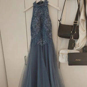 Blå långklänning med pärlor och fransar - Magisk blå långklänning med broderade blommor, pärlor och glittriga fransdetaljer på överdelen. Klänningen har hög hals, är ärmlös och har en voluminös tyllkjol som ger en riktigt elegant känsla. Perfekt för bal eller speciella tillfällen.   stl 42 men insydd till en Xs,S Går att sprätta upp lätt så en större kan har den med  800kr endast kap  Kostat ett par tusenlappar    ❤️❤️