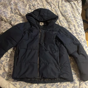 Mörkblå pufferjacka från McKinley - Snygg mörkblå pufferjacka från McKinley i storlek small. Jackan har huva, flera praktiska fickor med dragkedja och quiltad design. Perfekt för kalla dagar och har en clean look som funkar till de flesta stilar.