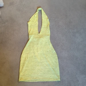 Grönl kortklänning med djup ringning - Snygg grön kortklänning med djup v-ringning och halterneck. Klänningen har en figurnära passform och är tillverkad i ett mjukt bomullsliknande material. 