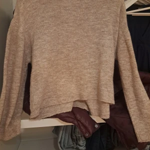 Beige stickad tröja från 157 - Mysig beige stickad tröja från 157 i storlek S. Tröjan har en enkel design med rund hals och långa ärmar, perfekt för att hålla dig varm under kyliga dagar. Den har en lätt loose passform och ribbade detaljer vid hals och muddar.