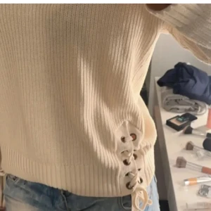 Stickad tröja med snörning - Beige stickad tröja med snygg snörningsdetalj i sidorna. Tröjan har lång ärm, ribbade muddar och en loose passform. Perfekt för lager-på-lager under höst och vinter. Supermjuk och enkel att matcha med jeans eller kjol.