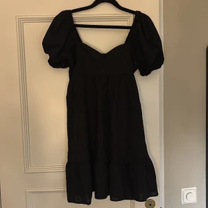 Svart linnéklänning från H&M Divided - Svart kortklänning i storlek M i linne från H&M Divided med puffärmar och söt hjärtformad urringning. Klänningen har smockad rygg och volang nertill för en trendig och luftig känsla. Aldrig använd då den var för stor och lappen är kvar☺️