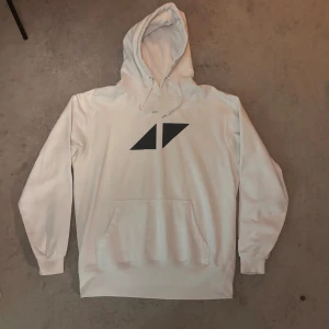  Avicii hoodie - Vit hoodie från Avicii med svart logga på bröstet. Klassisk känguruficka framtill, dragsko i huvan och långa ärmar. Mjuk och skön bomullsmix, perfekt för chill dagar eller när du vill ha en clean look.