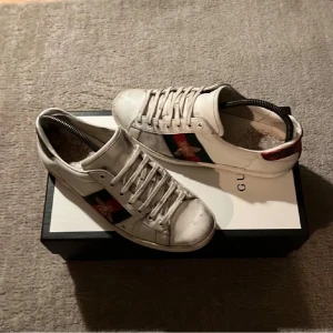Gucci Ace Bee - Tja! Säljer nu dessa riktigt feta Gucci Ace Bee skor! De är lite slitna, men annars väldigt bra skick och kritvita. Jag skulle säga att skicket är 7/10 just eftersom det är bara några få repor i lädret men annars jättebra skick. Storlek: 7,5 US, eller ca 40 - 41 EU👟. Nypris: 5000kr❌‼️ Mitt pris: 1099✅Allt OG följer med! Tveka inte att kontakta mig om du har frågor!🤝