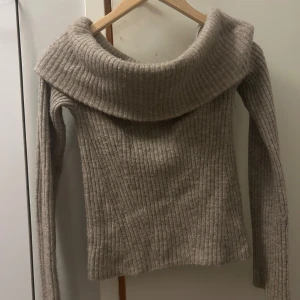 Beige ribbad stickad tröja - Säljer en beige stickad tröja med bred, nedvikt krage och ribbad struktur. Tröjan har långärmade ärmar och är perfekt för dig som gillar en chill och snygg look. Passar dig som vill ha något mjukt och varmt med lite loose fit.