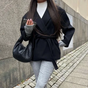 Svart kappa med bälte - Snygg svart kappa med omlott-design och matchande bälte i midjan. Materialet är mjukt och känns som ull, perfekt för höst och vinter. Enkel och stilren look som funkar till många outfits.