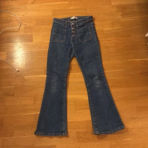 Blå  jeans med knappar - Snygga blå jeans med  passform och hög midja. Framtill finns stora fickor och flera synliga knappar som ger en cool vibration . Jeansen är tillverkade i klassiskt denimtyg och har en lätt utsvängd benform.🤣🫐🙈🙈🫐