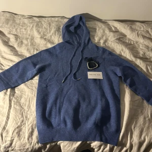 Grisch Blå Hoodie - Mysig blå stickad hoodie med huva och dragsko. Tröjan har långa ärmar och ribbade muddar vid ärmslut och nederkant. Perfekt för kyliga dagar när du vill vara både bekväm och snygg.