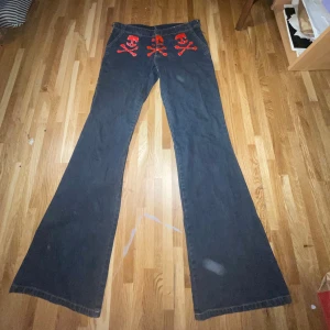 Asta Kask lågmidjade jeans - Jeans med Asta Kask-skallen fram och bak. De är utsydda på sidorna (bild 4). Målat dödskallarna själv men färgen håller i tvätten! Midjemått: 39cm, längd: 104cm, innerben: 82cm