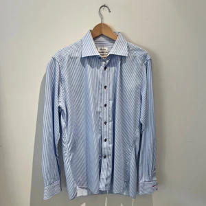 Blårandig skjorta från Stenströms - Snygg blårandig skjorta från Stenströms i storlek 43. Tillverkad i exklusiv twofold super cotton som känns mjuk och lyxig mot huden. Skjortan har klassisk krage, långa ärmar och mörka knappar framtill. Perfekt för dig som gillar stilrena detaljer och kvalitetsmaterial. Den är använd någon enstaka gång och det är bara att höra av er vid frågor