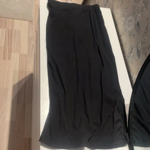 Svart ribbad långkjol från Shein - Svart långkjol från Shein med ribbad struktur och elastisk midja. Kjolen är enkel och stilren, perfekt för dig som gillar en clean look. Materialet är mjukt och följsamt, vilket gör den bekväm att bära hela dagen.