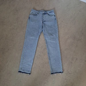 Ljusblå raka jeans med råa kanter - Säljer ett par ljusblå jeans med raka ben och snygga råa, fransiga kanter nertill. Klassisk femficksmodell med hög midja och bälteshällor. Perfekta för en avslappnad och trendig look.