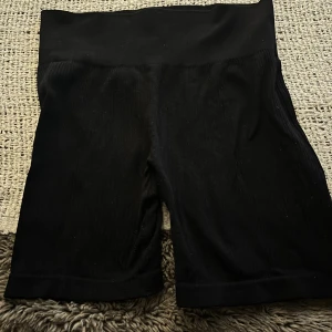Svarta cykelshorts med hög midja - Svarta, tighta cykelshorts med hög midja och ribbad struktur. Perfekta för träning eller en chill vardagslook. Mjukt och stretchigt material som sitter skönt på kroppen.