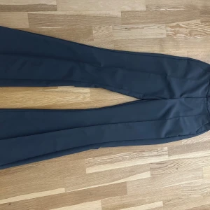 Svarta kostymbyxor med pressveck från bikbok - Snygga svarta kostymbyxor med klassiskt pressveck och raka ben. Byxorna har hög midja och en stilren design med diskreta fickor bak. Perfekta för en clean och dressad look. Materialet känns mjukt och har en lätt glans.