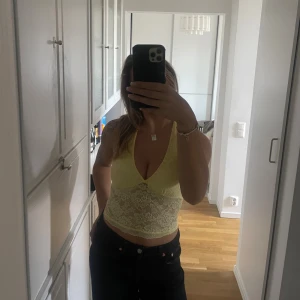 Gul spetsig croppad linnetopp - Säljer en ljusgul croppad linnetopp med spetsdetaljer och v-ringad hals. Toppen har smala axelband och är tillverkad i ett mjukt, transparent spetsmaterial som ger en fräsch och somrig vibe. Perfekt för dig som gillar att sticka ut med färg och detaljer.