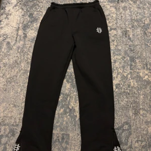 Svarta mjukisbyxor  - Svarta mjukisbyxor med vit broderad logga på höften och vid benslutet. Byxorna har elastisk midja, raka ben. Perfekta för chill eller streetwear. Jette skönt material o passar alla stillar