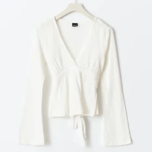 Vit omlottopp - Säljer en fräsch vit omlottopp från Monki med v-ringning och långa ärmar. Toppen har knyt i midjan och är tillverkad i ett mjukt, lätt strukturerat material som ger en skön känsla. Perfekt för dig som gillar stilrena och enkla plagg.