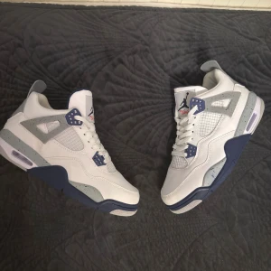 Nike Air Jordan 4 White Navy - Nike Air Jordan 4 sneakers i vitt skinn med marinblå och grå detaljer. Sulan har stänk i grått och inslag av rött undertill. Klassisk Jumpman-logga på plösen och hälen, meshpaneler och snörning. Snygg retrostil med platt sula och rund tå. Skorna använda ett få tal gånger. Kommer inte med orginal box.